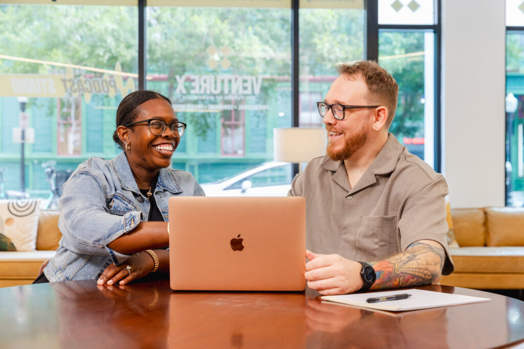Tranceform Wellness' founder Benjamin Howell sits with a new patient, a laptop between them. Together, they are walking through the steps of virtual psychiatry services in Orlando, both smiling.