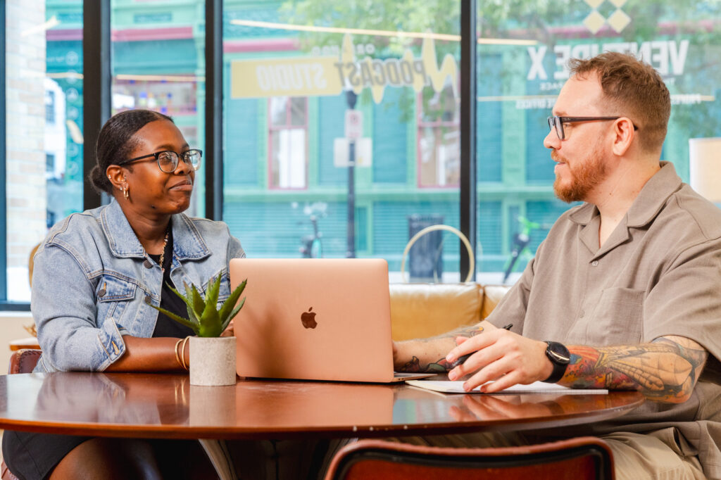A new patient and Tranceform Wellness' founder Benjamin Howell sit at a desk with a laptop between them. Together, they are walking through the steps of virtual psychiatry services in Orlando, both smiling.